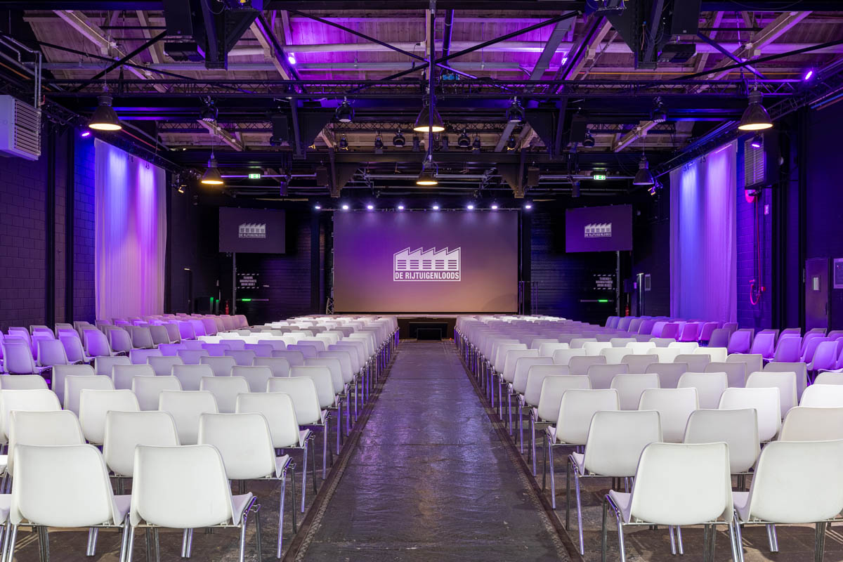 Grote plenaire zaal in De Rijtuigenloods met theateropstelling en podium voor congres of presentatie