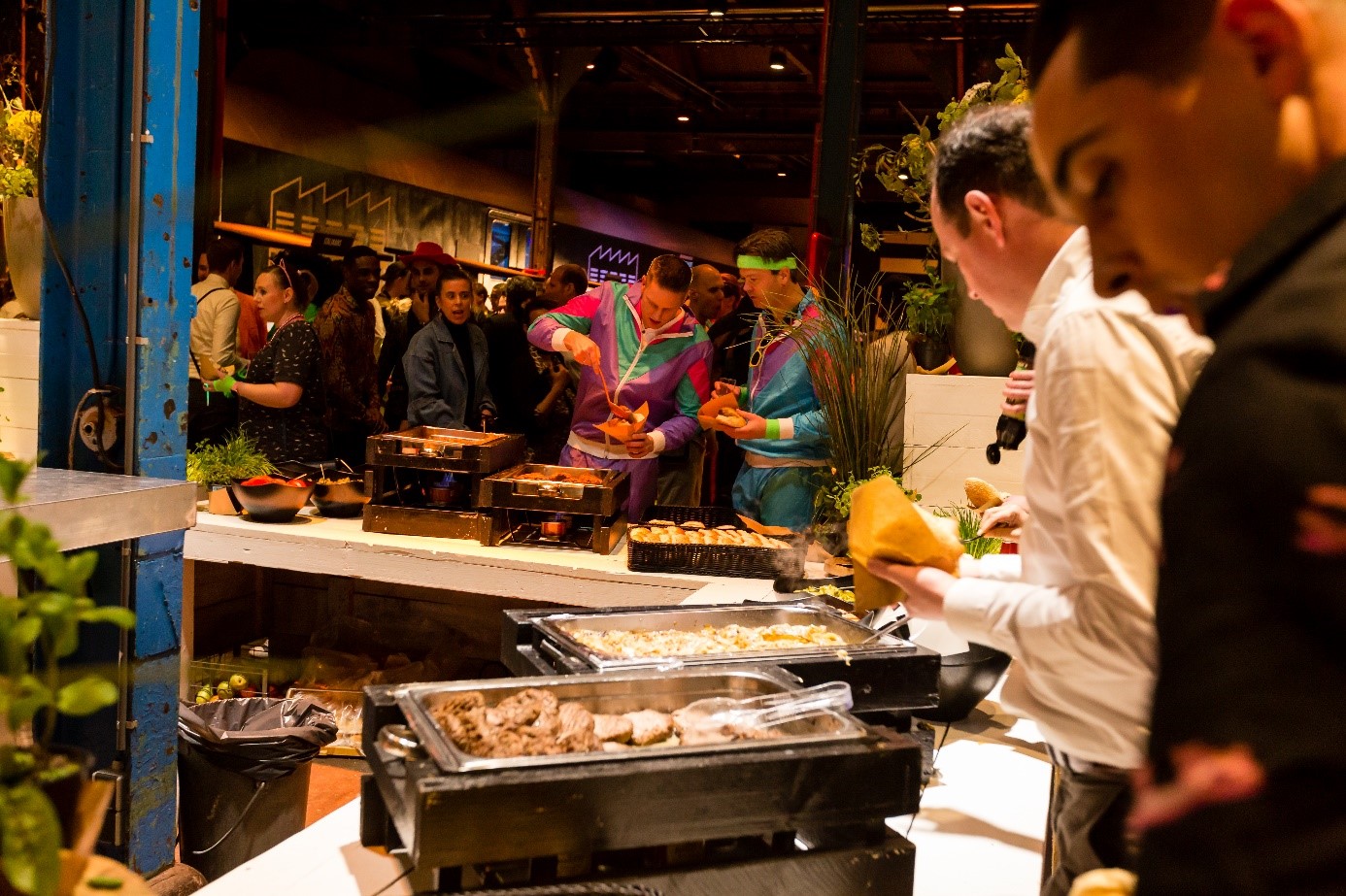 Gasten genieten van foodstations en catering tijdens een bedrijfsfeest in De Rijtuigenloods.