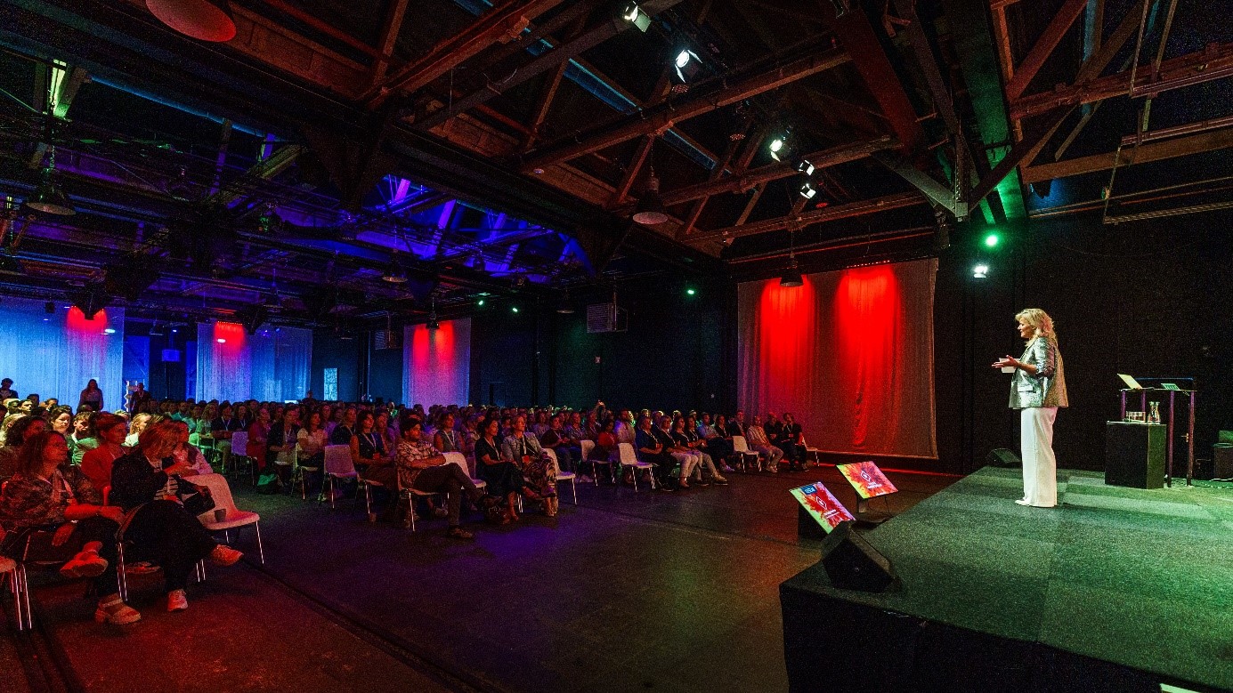 Spreker op het podium tijdens een congres in De Rijtuigenloods in Amersfoort met een grote plenaire zaal.